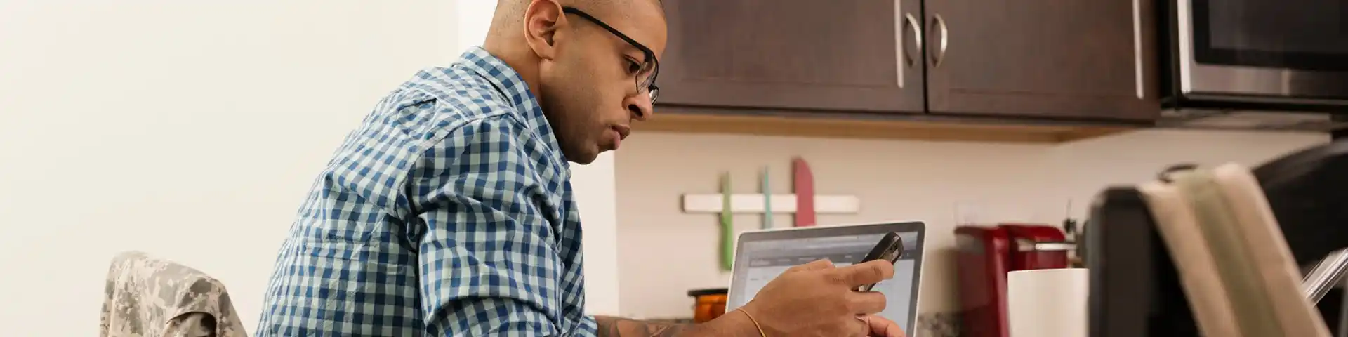 man looking at his phone with his laptop next to him